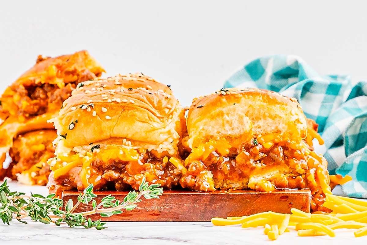 Τρεις τυρένιες μικρές πίτες Sloppy Joe σε ξύλινη επιφάνεια, γαρνιρισμένες με φρέσκα μυρωδικά. Στο φόντο διακρίνεται ένα καρό ύφασμα.