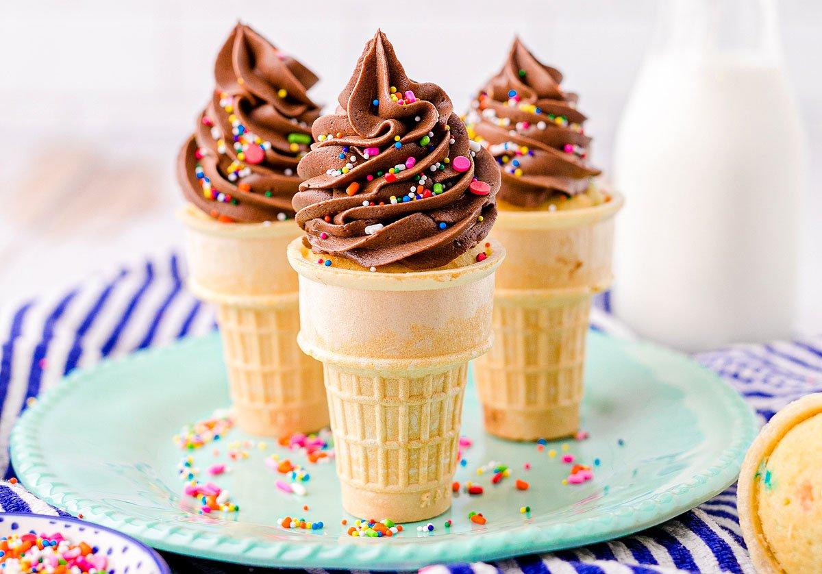 Τρία cupcakes σε χωνάκι παγωτού με σοκολατένια βουτυρόκρεμα και πολύχρωμη τρούφα βρίσκονται σε ένα πράσινο πιάτο δίπλα σε ένα μπουκάλι γάλα – τέλεια cupcakes για πάρτι γενεθλίων.