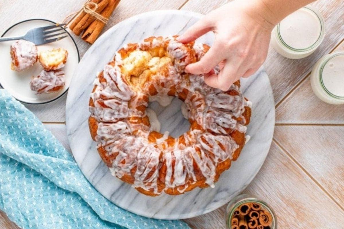 Ένα άτομο δαγκώνει ένα ψωμάκι κανέλας Pillsbury σε ένα πιάτο.