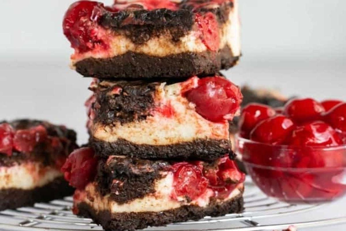 Μια στοίβα από μπάρες σοκολάτας κερασιού cheesecake σε σχάρα ψύξης, ιδανικές για τους λάτρεις των επιδορπίων που αναζητούν απολαυστικές συνταγές σοκολάτας με κεράσι.