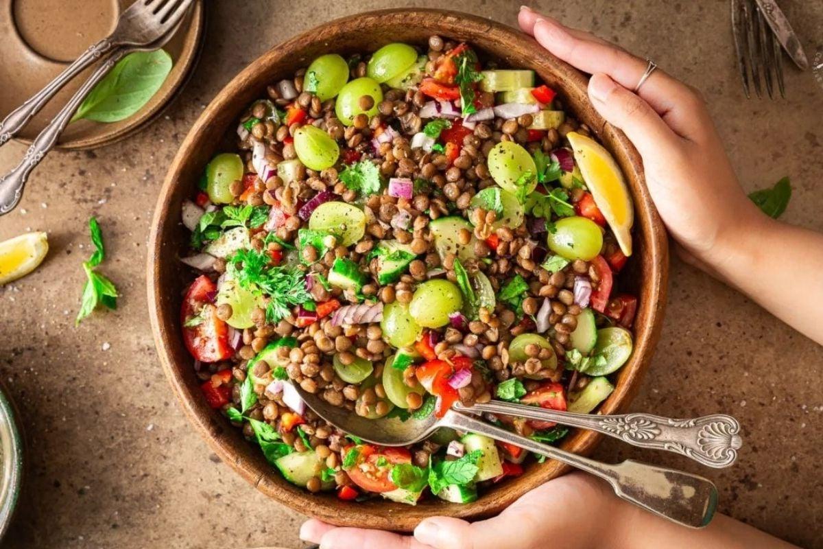 A person holding a bowl of lentil salad with grapes, a perfect choice for potluck sides.