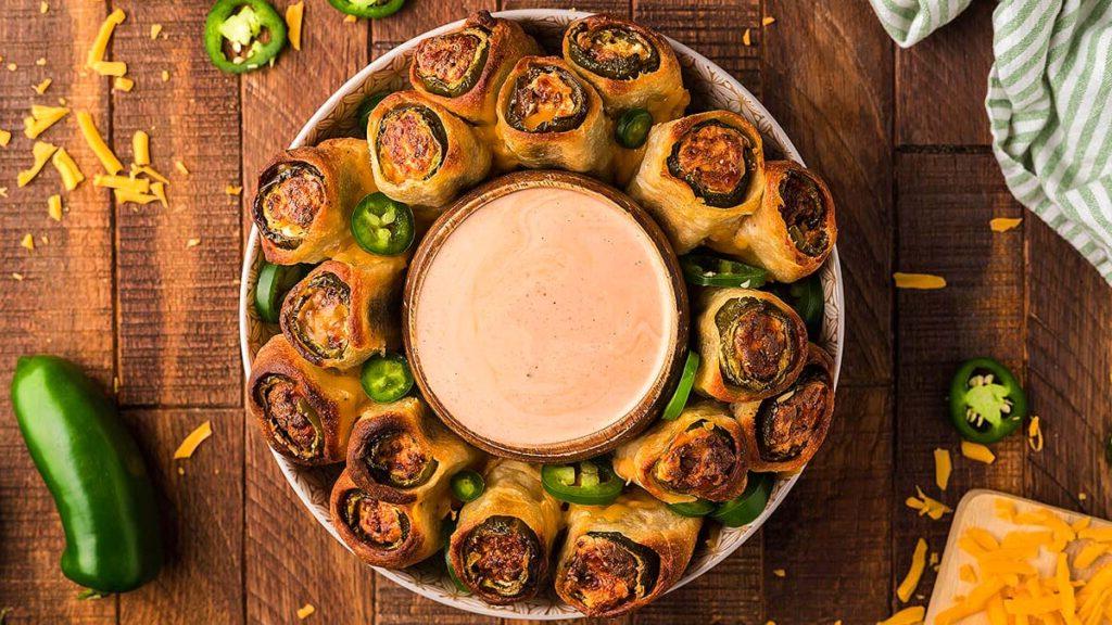 Ρολάκια Jalapeño popper σε πιάτο με μπολ ντιπ.