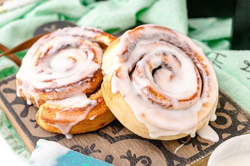 Two cinnamon rolls on a board with frosting.