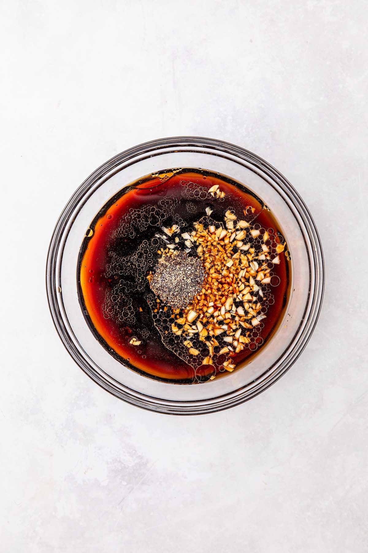 A bowl featuring a dark, savory liquid reminiscent of slow cooker Mongolian beef, with chopped nuts adding texture and a small mound of ground black pepper crowning the dish.