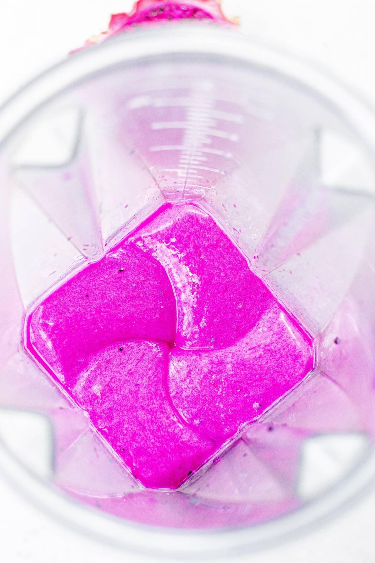 Φωτεινό ροζ smoothie που αναμειγνύεται σε ένα διάφανο μπλέντερ, από πάνω—μια ζωντανή συνταγή χρησιμοποιώντας dragon fruit που είναι τόσο εντυπωσιακή όσο ένα πολύχρωμο παγωτό.