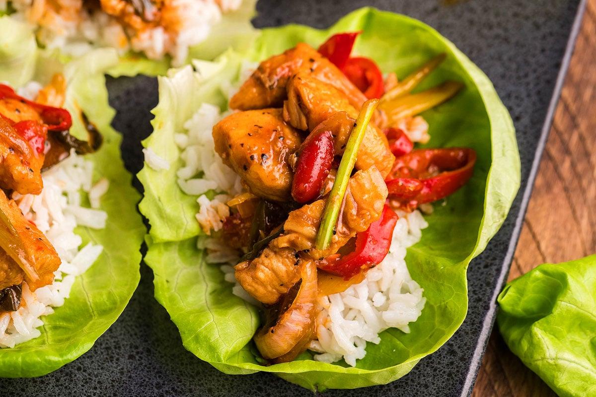 Gochujang κοτόπουλο και stir-fry λαχανικών σερβιρισμένο σε φρέσκα φύλλα μαρουλιού με μια στρώση λευκού ρυζιού και μια γλυκιά και πικάντικη σάλτσα.