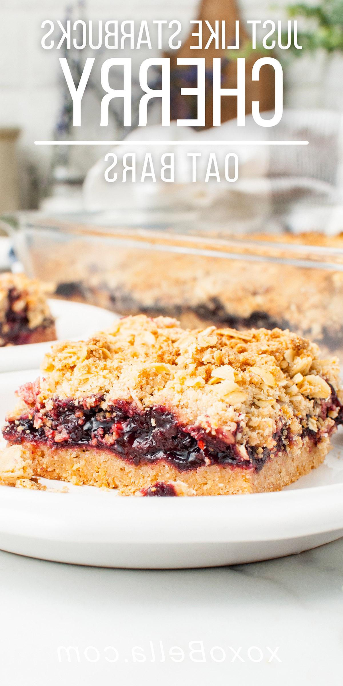 Μια μπάρα βρώμης με κεράσι και επικάλυψη crumble βρίσκεται σε ένα πιάτο, εμπνευσμένη από μια συνταγή copycat της Starbucks, με περισσότερες μπάρες κερασόπιτας και ένα ταψί στο παρασκήνιο—τέλεια φτιαγμένες με κατεψυγμένα κεράσια.