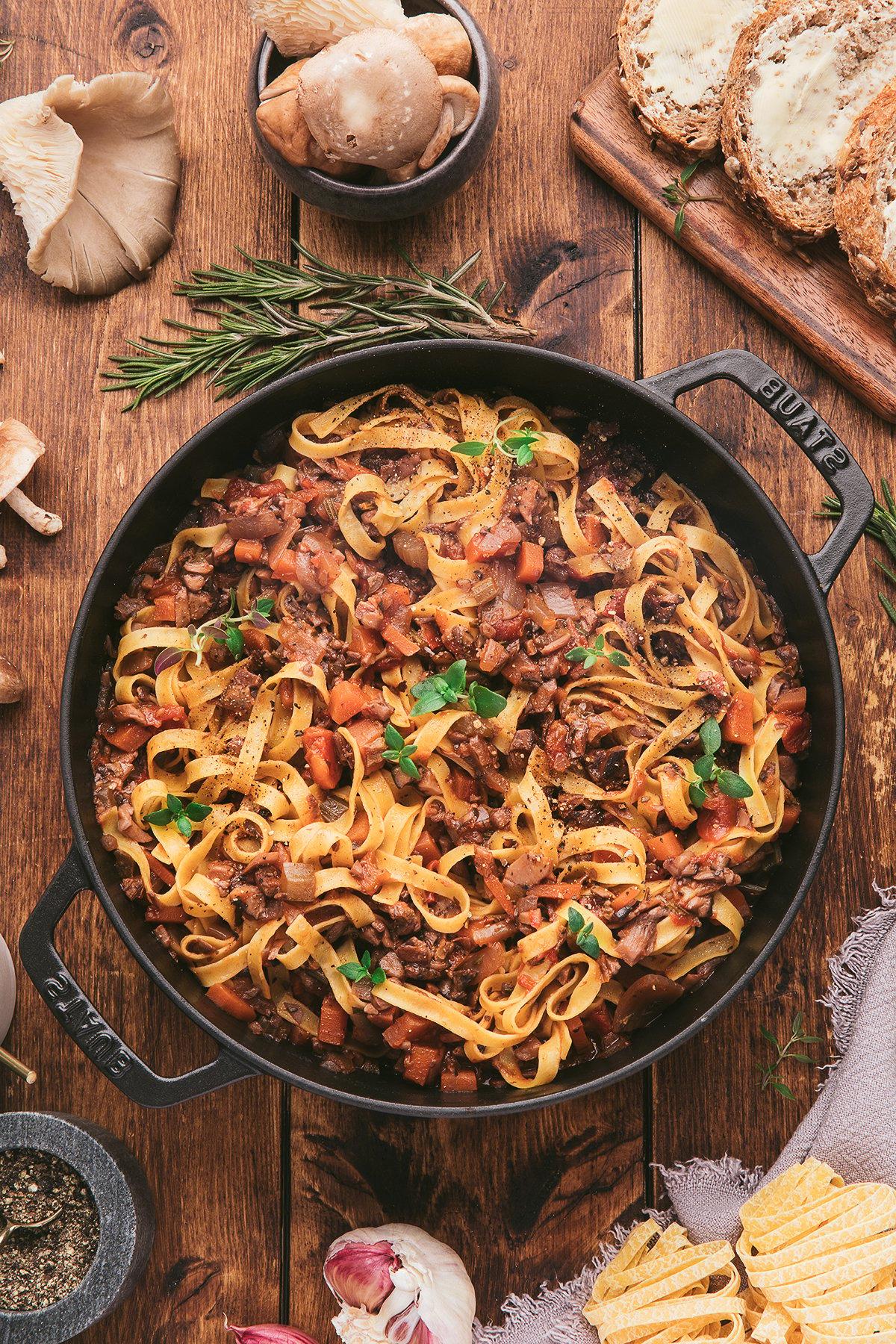 Τα tagliatelle ζυμαρικά με αλμυρό ραγού χωρίς κρέας – μια σπιτική σάλτσα σπαγγέτι με μανιτάρια και λαχανικά – σερβιρισμένα σε ένα μαύρο τηγάνι πάνω σε ένα ρουστίκ ξύλινο τραπέζι.