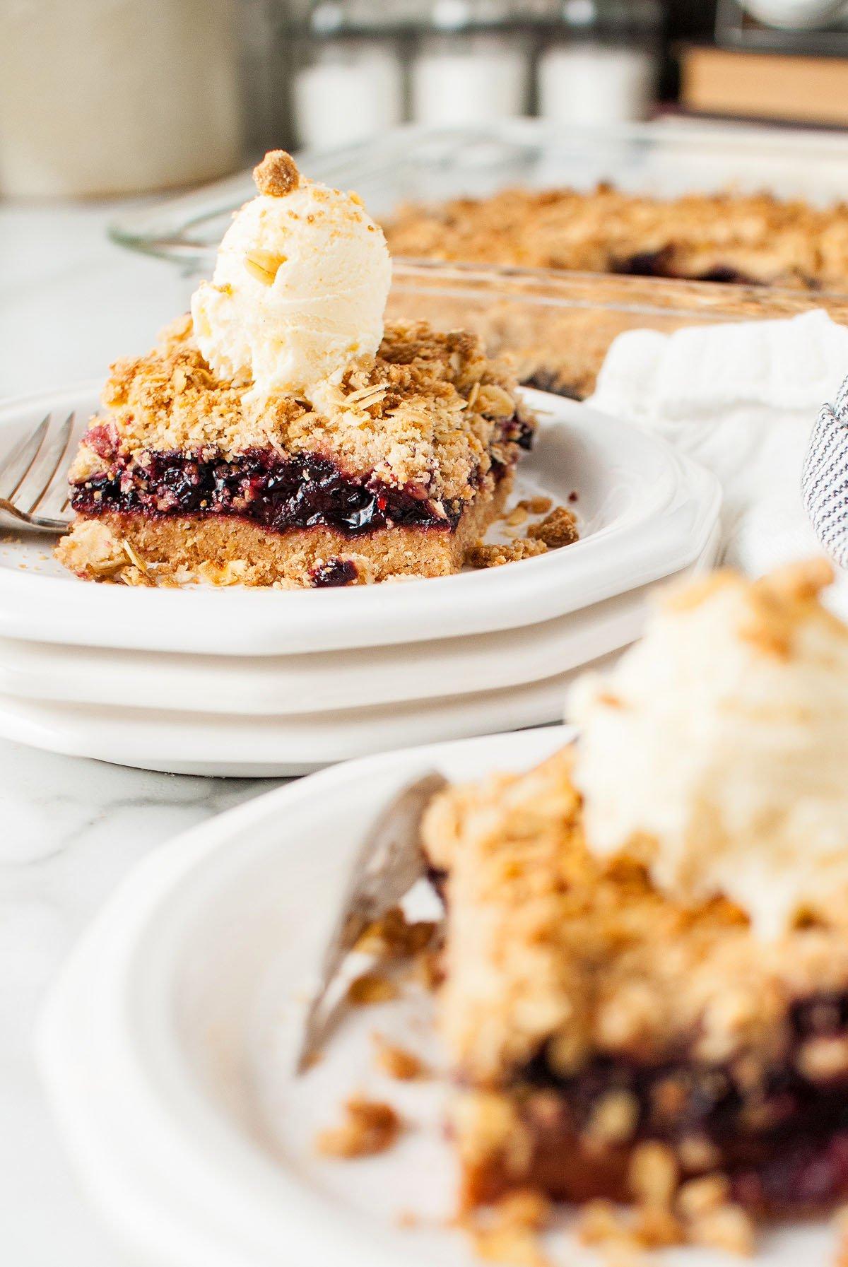 Μια φέτα από crumble με μούρα, εμπνευσμένη από τις μπάρες βρώμης με κεράσι Michigan τύπου Starbucks, με παγωτό βανίλια και ένα πιρούνι σε ένα λευκό πιάτο.