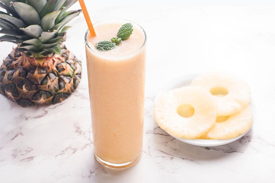 Ένα φρέσκο smoothie ανανά-ροδάκινου με καλαμάκι και μια φέτα ανανά.