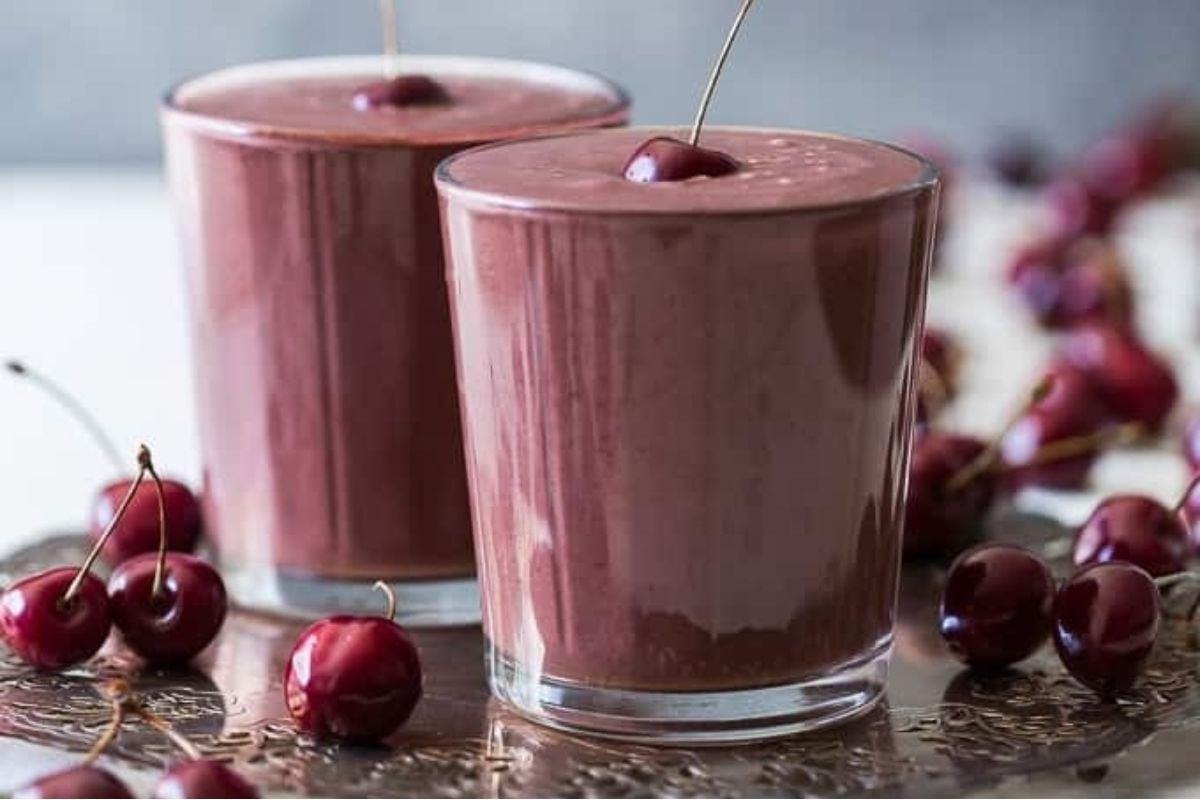 Δύο ποτήρια smoothie με κεράσια στην κορυφή, ιδανικά για μια δροσιστική σοκολατένια απόλαυση με κεράσι.