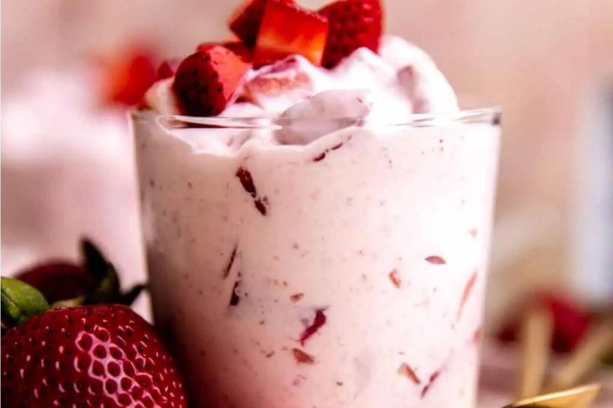 Ένα ροζ smoothie φράουλας σε ποτήρι με σαντιγί και φράουλες.