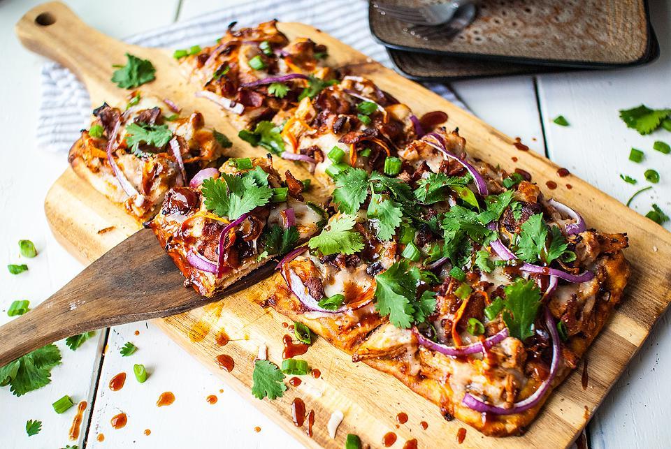 Μια πίτσα flatbread σε ξύλο κοπής με μια φέτα να αφαιρείται.