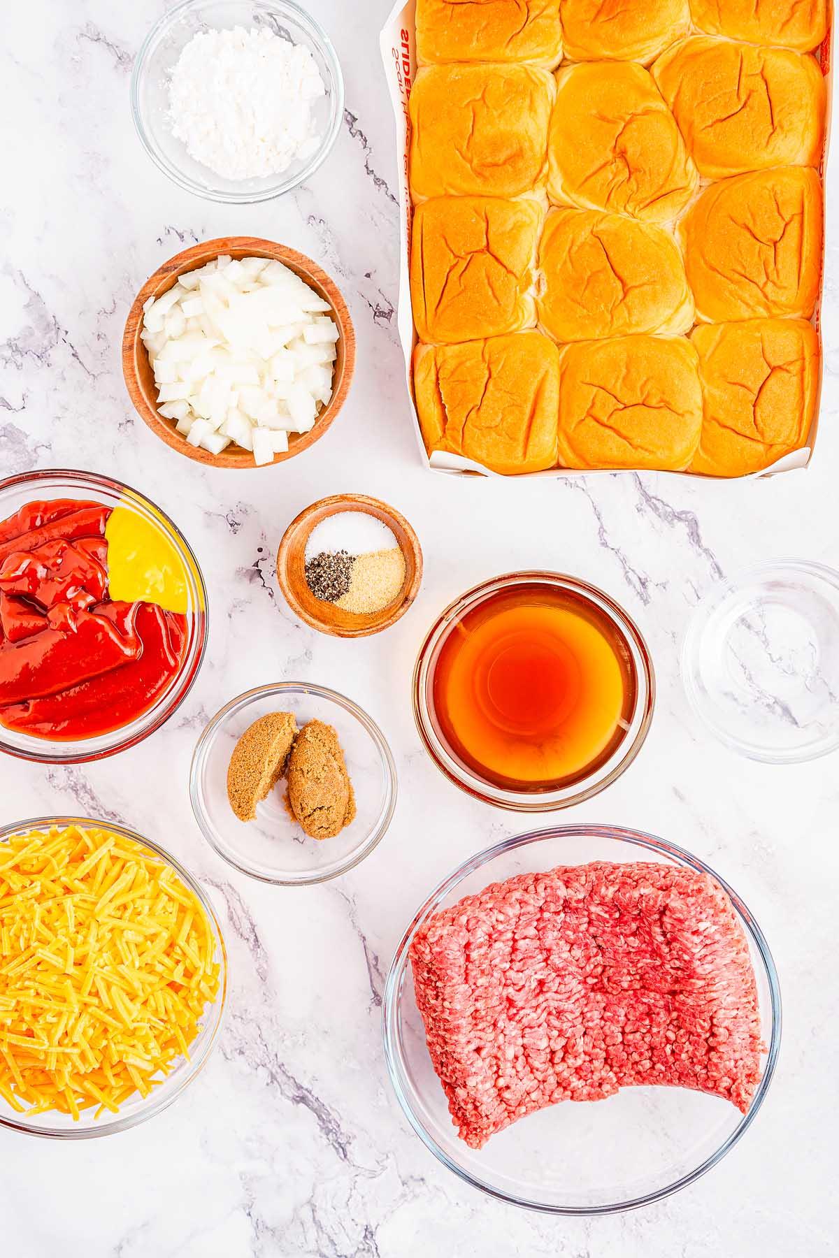 Υλικά για νόστιμα Sloppy Joe sliders τοποθετημένα σε μαρμάρινη επιφάνεια, συμπεριλαμβανομένων ψωμιών slider, ψιλοκομμένων κρεμμυδιών, τριμμένου τυριού, κιμά, κέτσαπ, μουστάρδας, καστανής ζάχαρης, σάλτσας Worcestershire, κορν φλάουρ, σκόνης σκόρδου, μαύρου πιπεριού και αλατιού.