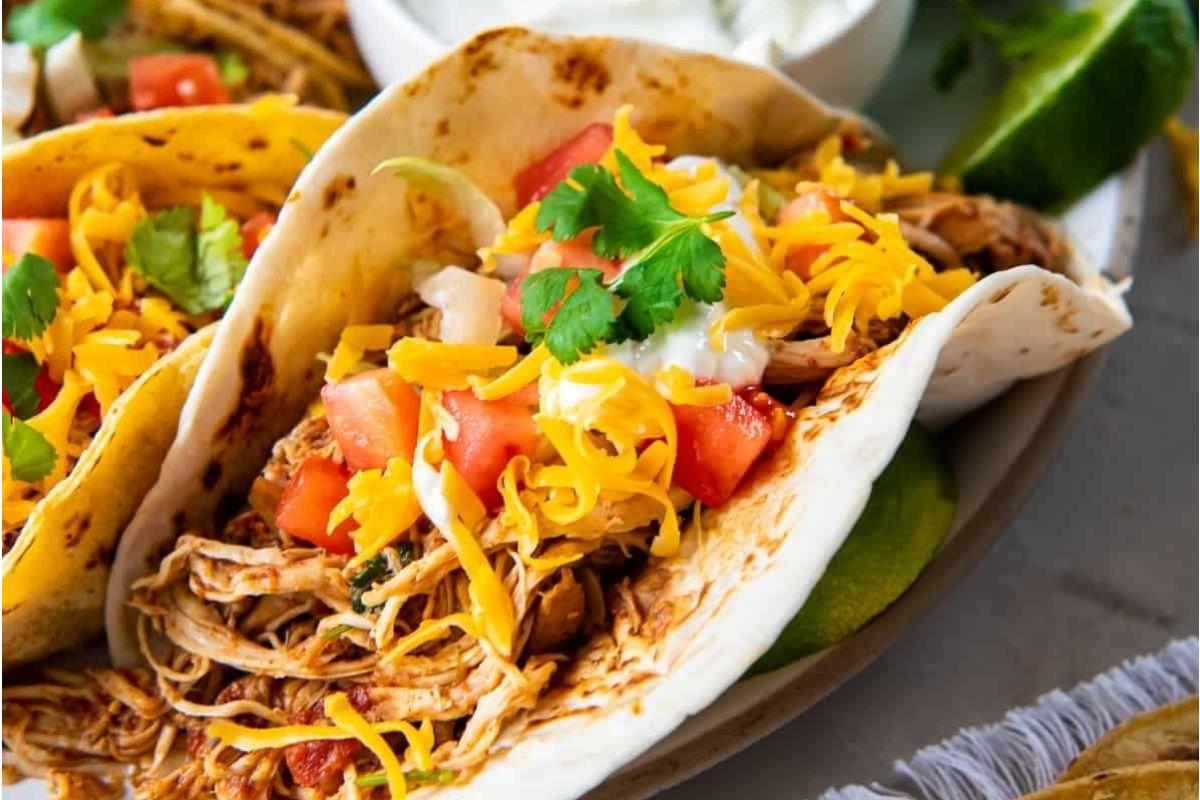 Κοντινό πλάνο ενός νόστιμου taco γεμάτου με τεμαχισμένο κοτόπουλο, τριμμένο τυρί, κομμένες ντομάτες, κόλιανδρο και ξινή κρέμα, τυλιγμένο σε μια μαλακή τορτίγια — μια τέλεια επιλογή για όσους αναζητούν λαχταριστές συνταγές κοτόπουλου.