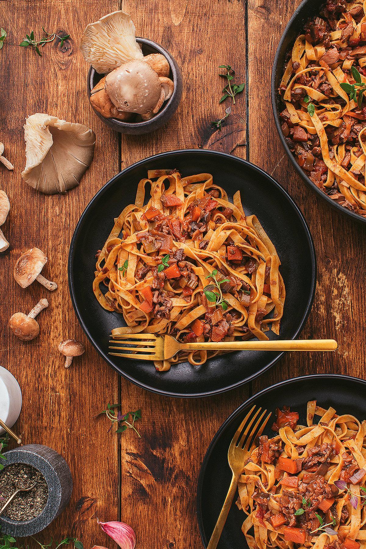 Τα tagliatelle ζυμαρικά με ένα αλμυρό ραγού χωρίς κρέας από μανιτάρια και λαχανικά σε μαύρα μπολ πάνω σε ένα ξύλινο τραπέζι, γαρνιρισμένα με βότανα.