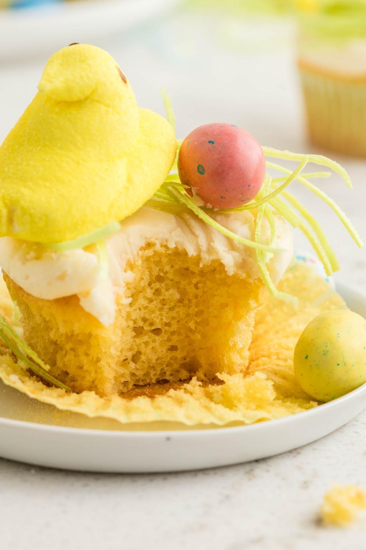 Cupcake με κίτρινο γλάσο, στολισμένο με ένα κίτρινο ζαχαρωτό σε σχήμα κοτόπουλου και πολύχρωμα ζαχαρωτά αυγά σε πράσινες κλωστές. Ένα μεγάλο κομμάτι λείπει από το cupcake.