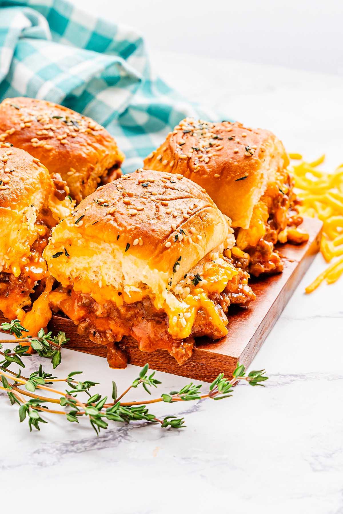 Τρεις τυρένιες μικρές πίτες Sloppy Joe γεμιστές με κιμά σε ξύλινη επιφάνεια, με τριμμένο τυρί και ένα μπλε και λευκό καρό ύφασμα στο φόντο.