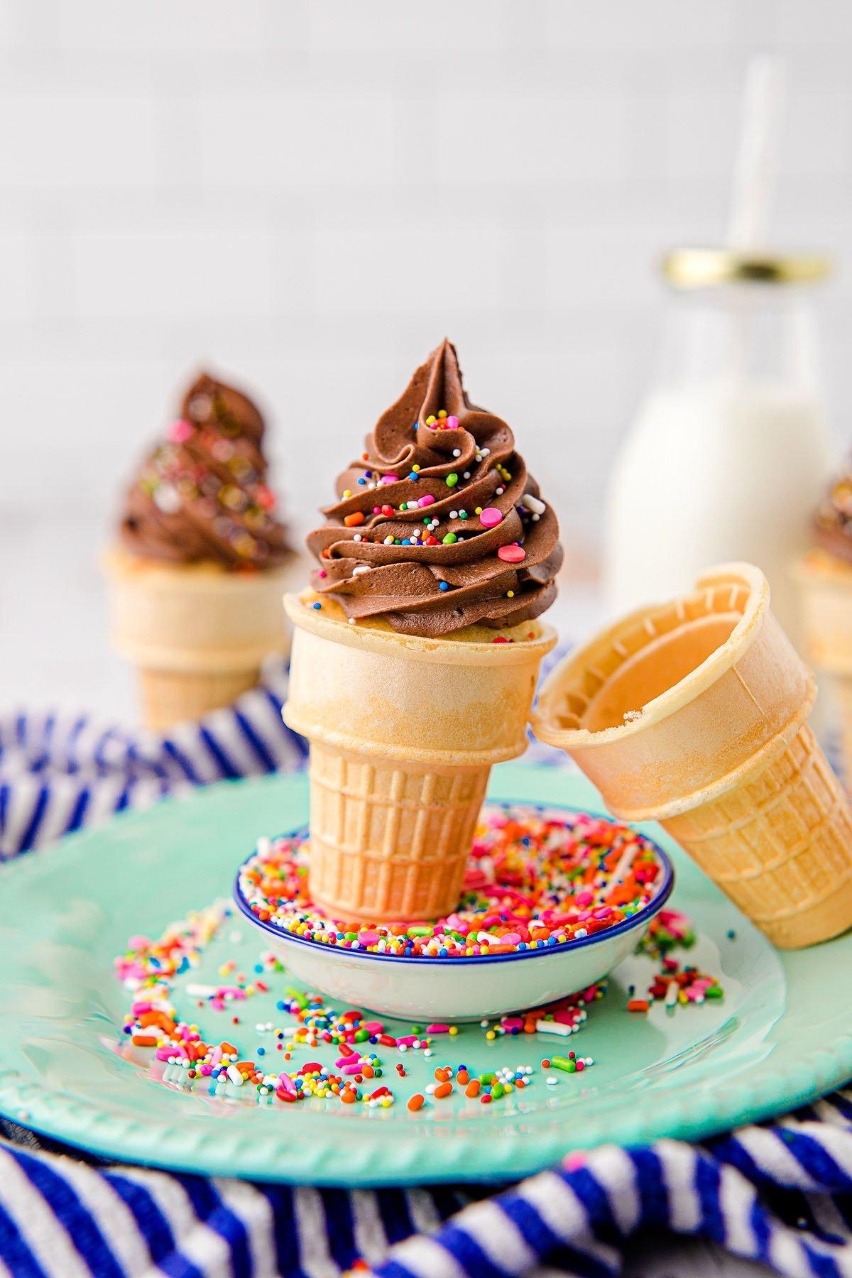 Cupcakes με επικάλυψη σοκολάτας σε χωνάκια παγωτού με πολύχρωμη τρούφα σε πιάτο, και ένα μπουκάλι γάλα στο παρασκήνιο – τέλειες λιχουδιές εμπνευσμένες από το μείγμα funfetti για πάρτι γενεθλίων.