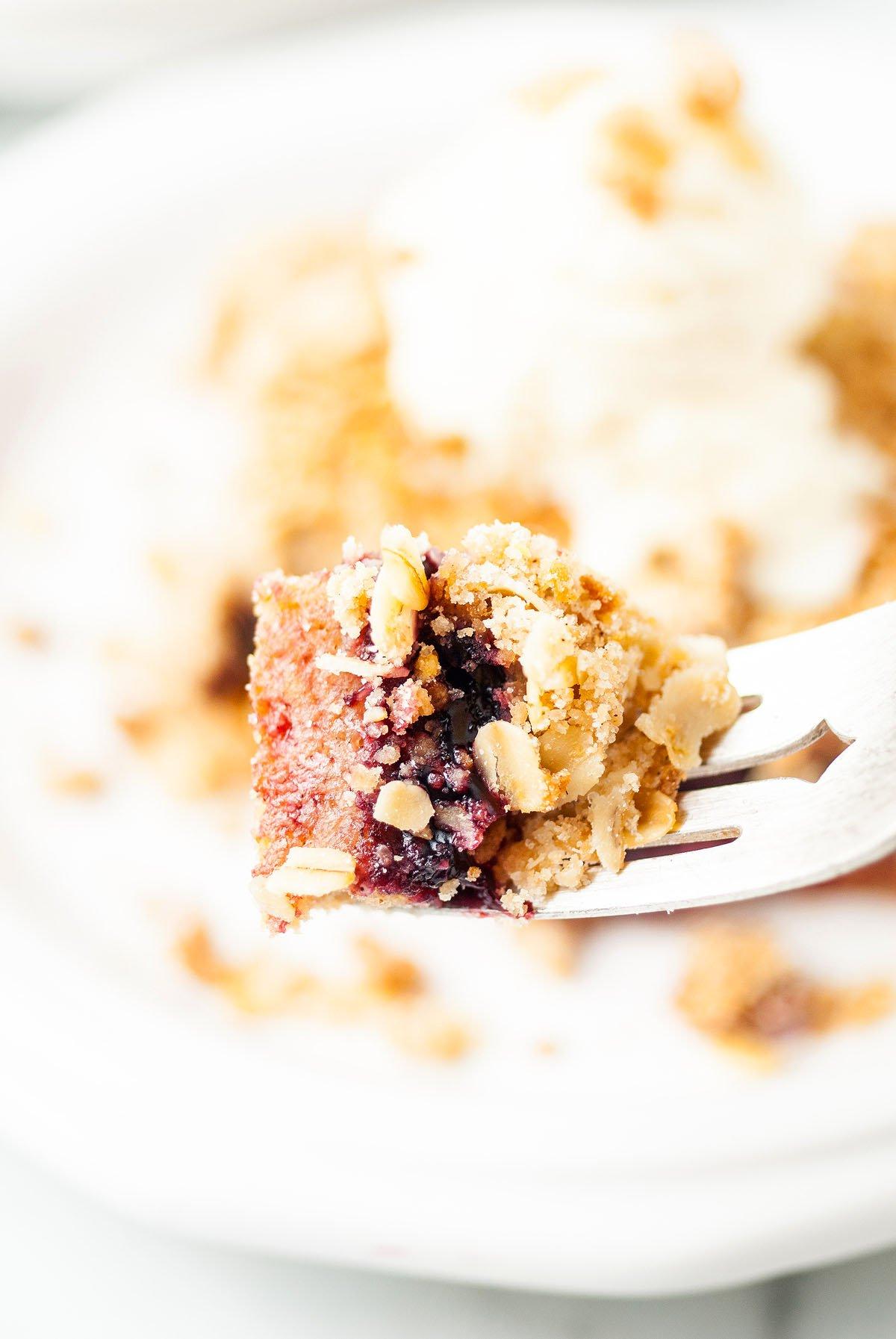 Ένα πιρούνι κρατάει μια μπουκιά από crumble μούρων με βρώμη, που θυμίζει τις μπάρες βρώμης με κεράσι Michigan τύπου Starbucks, με περισσότερο crumble και παγωτό θολό στο παρασκήνιο.