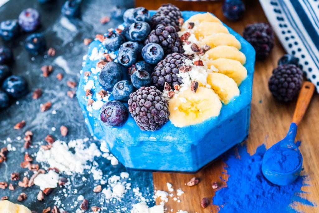 Ένα μπλε smoothie σε μπολ με φρέσκα φρούτα από πάνω.