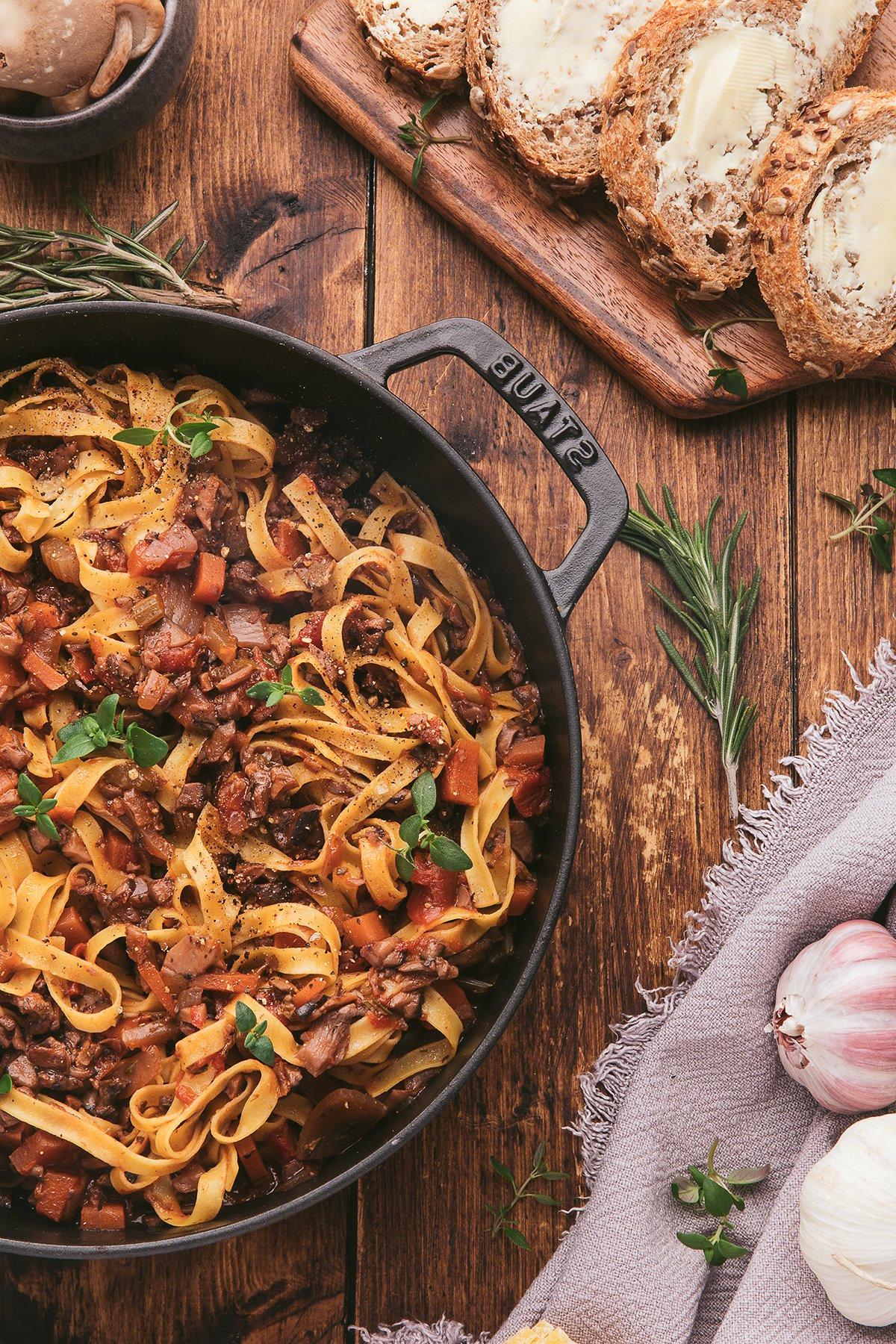 Τα tagliatelle ζυμαρικά με σπιτική σάλτσα σπαγγέτι με μανιτάρια, σερβιρισμένα σε ένα τηγάνι μαζί με ψιλοκομμένο ψωμί, σκόρδο και φρέσκα βότανα πάνω σε ένα ξύλινο τραπέζι.