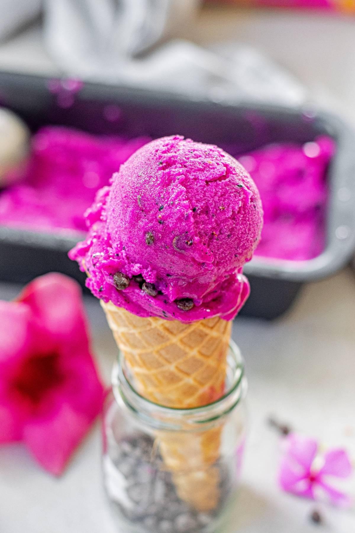 Ζωντανό ροζ παγωτό Dragon Fruit σε χωνάκι βάφλας, τοποθετημένο σε ένα γυάλινο βάζο, με θολό φόντο—ένα δροσιστικό παγωμένο επιδόρπιο χωρίς γαλακτοκομικά.