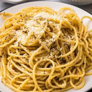 Ένα πιάτο cacio e pepe, με σπαγγέτι γαρνιρισμένα με τριμμένο τυρί και μια πρέζα μαύρο πιπέρι, είναι όμορφα τοποθετημένο σε ένα λευκό πιάτο με ένα πιρούνι κοντά.