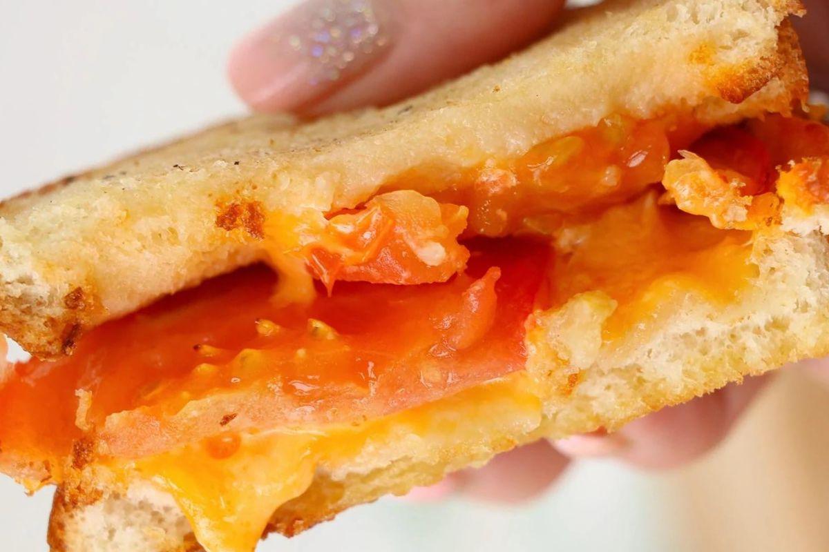 Κοντινό πλάνο συνταγών για grilled cheese που δείχνουν ένα σάντουιτς με λιωμένο τυρί και φέτες ντομάτας.