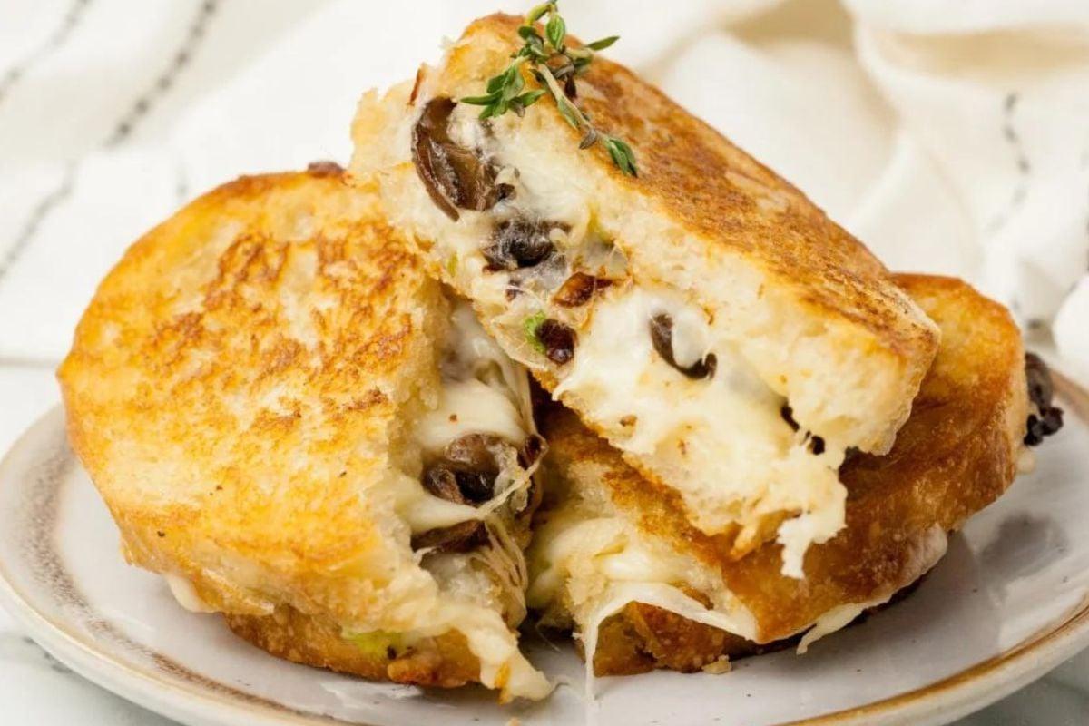 Ένα σάντουιτς grilled cheese με λιωμένο τυρί και μανιτάρια σε ένα πιάτο, τέλειο για να δοκιμάσετε νέες συνταγές grilled cheese.