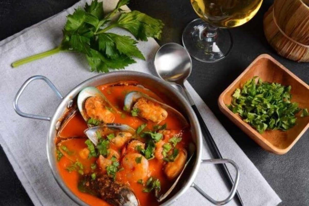 Ένα γεύμα επτά ψαριών, συμπεριλαμβανομένου ενός μπολ θαλασσινής σούπας με ένα ποτήρι κρασί δίπλα του.