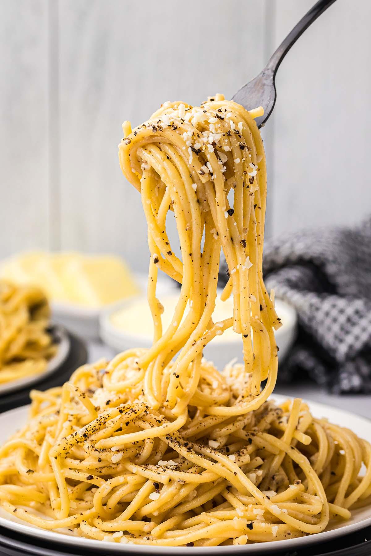 Ένα πιρούνι σηκώνει μια μερίδα cacio e pepe, με σπαγγέτι κομψά γαρνιρισμένα με τριμμένο τυρί και πιπέρι, από ένα πιάτο.