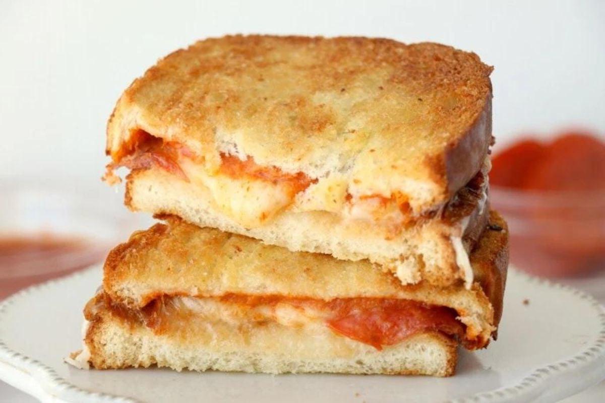 Συνταγές για σάντουιτς grilled cheese με λιωμένο τυρί και ντομάτα, κομμένο στη μέση σε ένα πιάτο.
