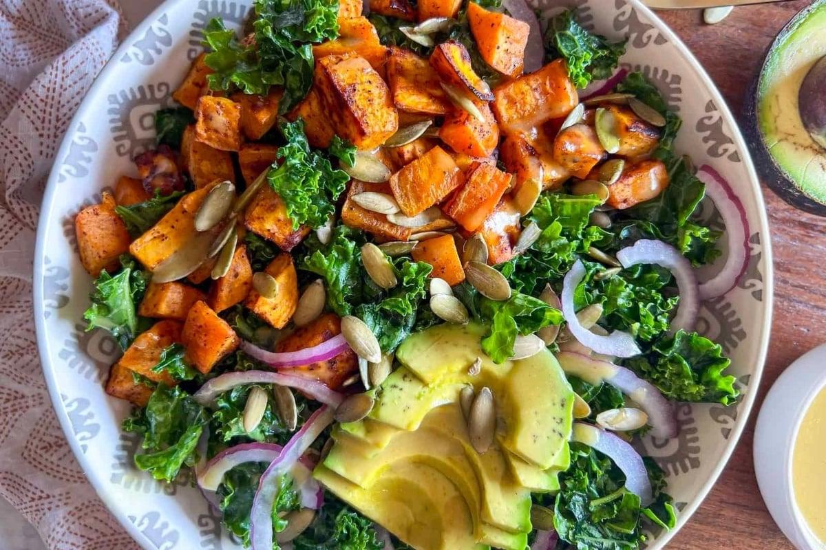 Ένα πιάτο με σαλάτα κέιλ και γλυκοπατάτας με dressing αβοκάντο, ιδανική για ένα υγιεινό δείπνο.