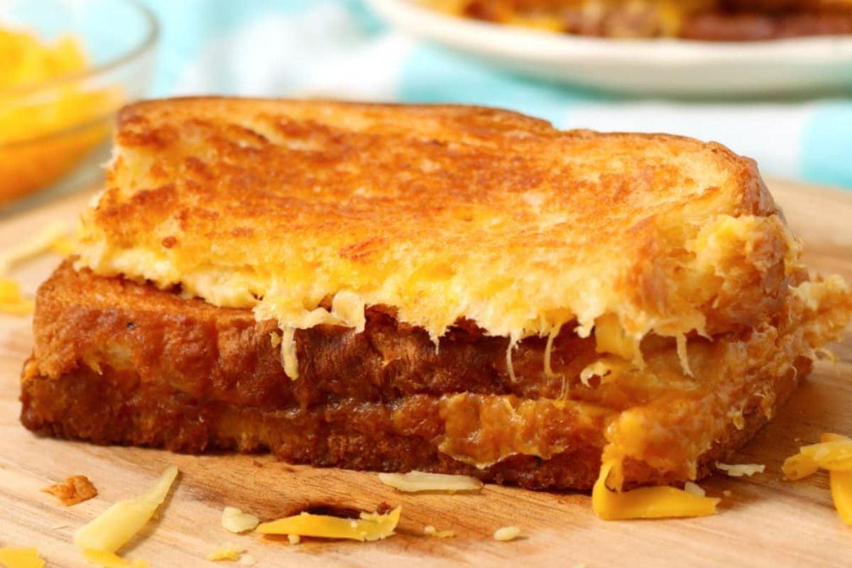 Ένα χρυσαφένιο-καφέ σάντουιτς grilled cheese σε ξύλινο ταμπλό με λιωμένο τυρί ορατό στις πλευρές, τέλειο για συνταγές grilled cheese.