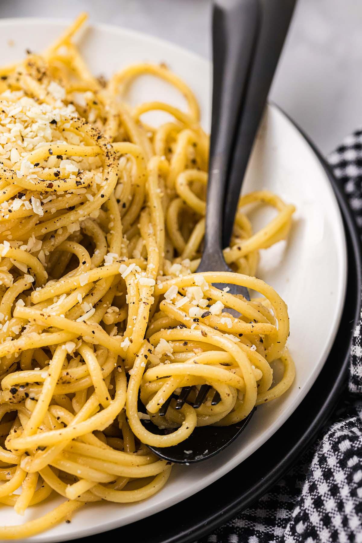Ένα πιάτο κλασικό cacio e pepe, με τέλεια μαγειρεμένα σπαγγέτι διακοσμημένα με ψιλοτριμμένο τυρί και μια δόση μαύρου πιπεριού, σερβιρισμένο κομψά με ένα πιρούνι.