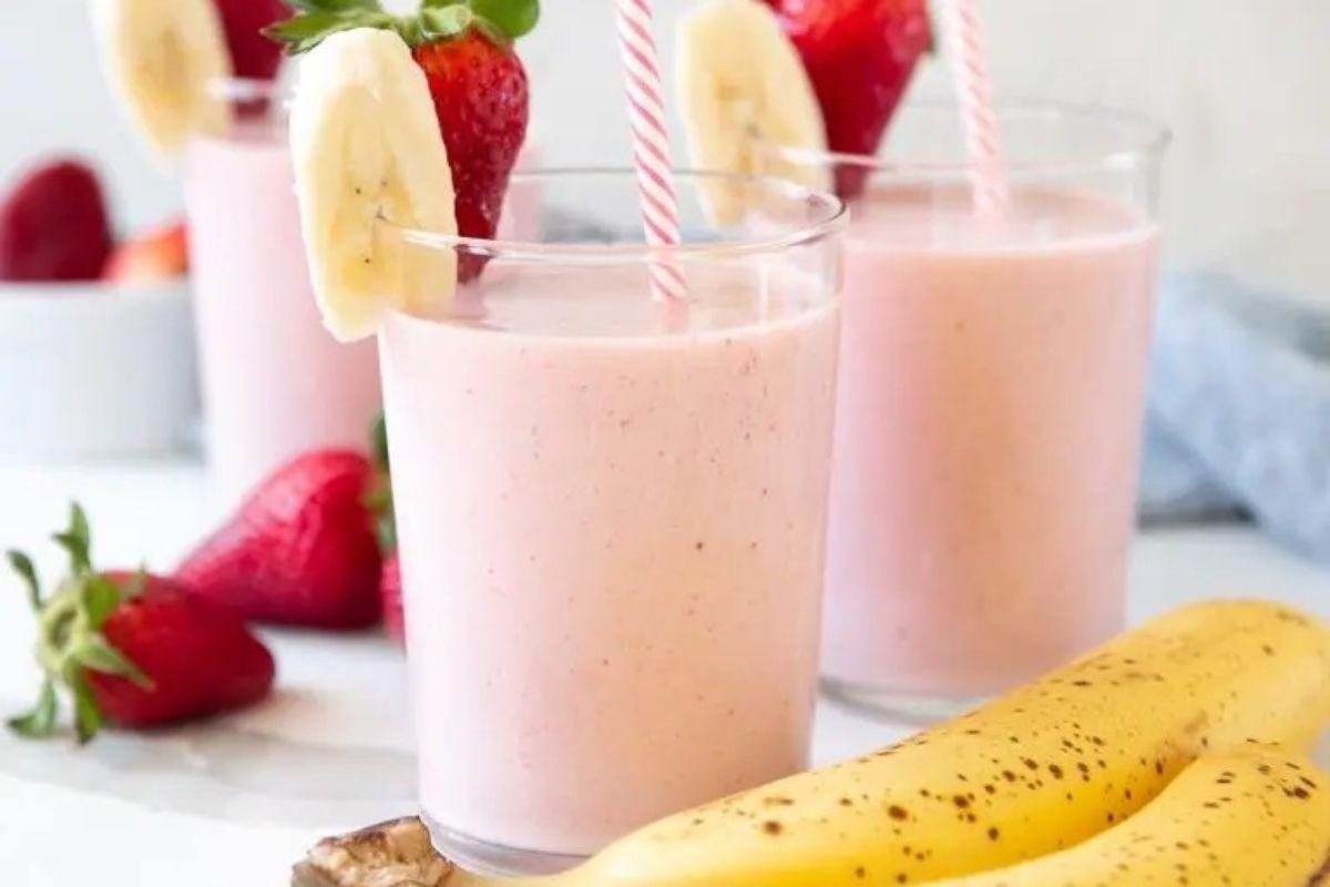 Ένα κρεμώδες smoothie φράουλας και μπανάνας σε ποτήρι, με φρέσκα φρούτα γαρνιτούρα.