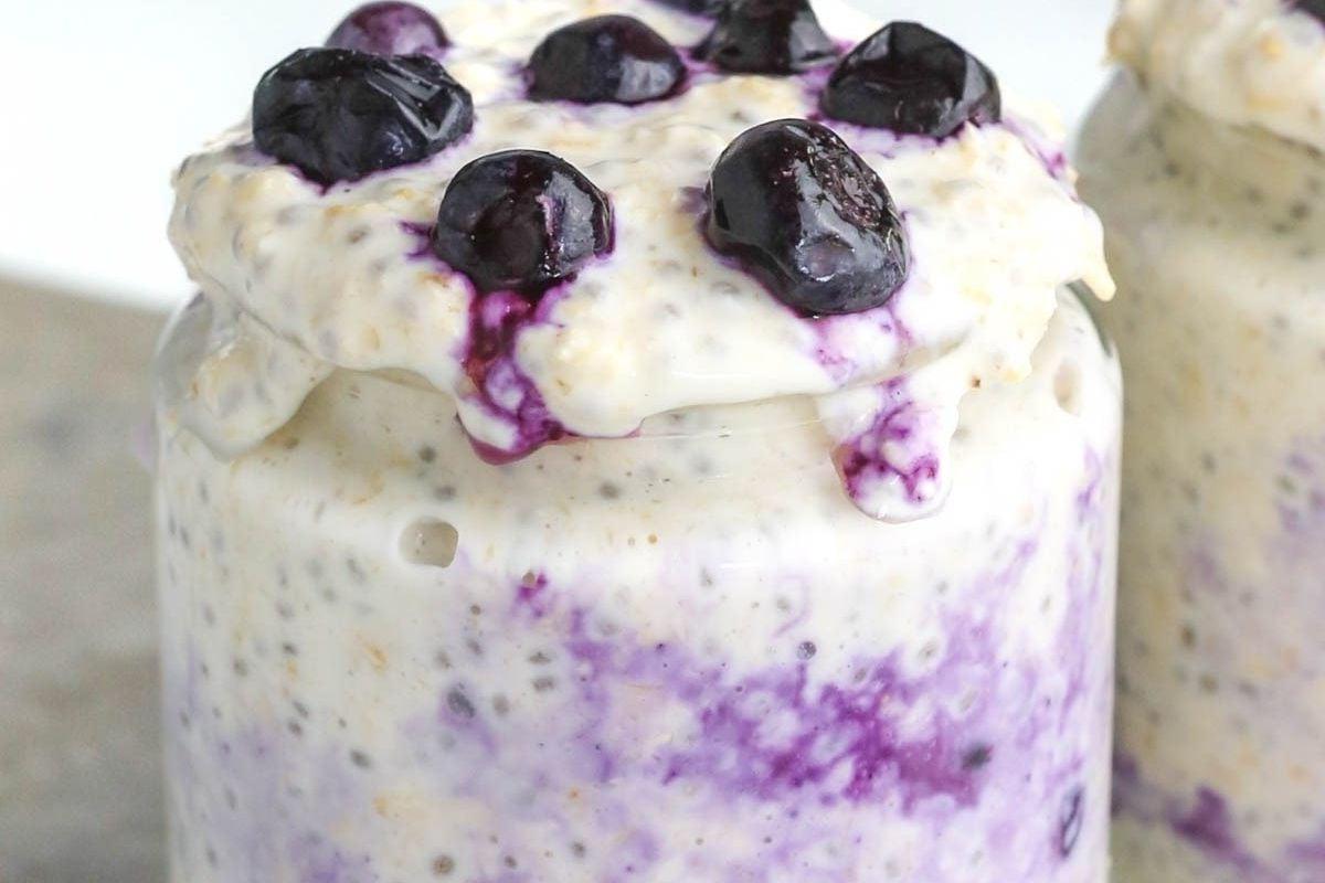 Ένα ποτήρι με overnight oats cheesecake μύρτιλου, στρωμένο με βρώμη, μύρτιλα και κρεμώδες τυρί.
