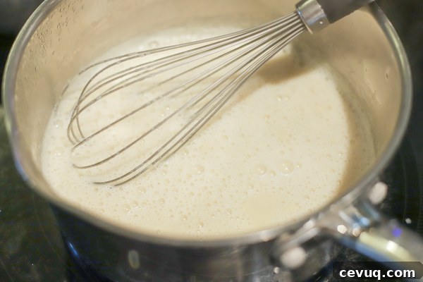 simmering milk, cream, and maple syrup in a saucepan with a whisk