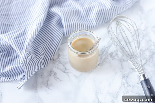 homemade sweetened condensed milk in a jar with a whisk to the right
