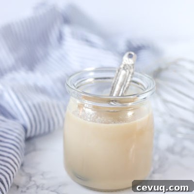 glass jar of homemade sweetened condensed milk with an antique silver spoon coming out. a blue and white striped towel is in the background