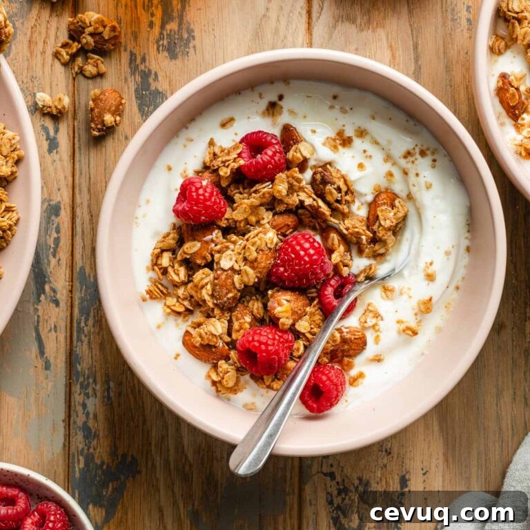 Overhead view of honey almond granola with yogurt and raspberries in a pink bowl with a spoon.