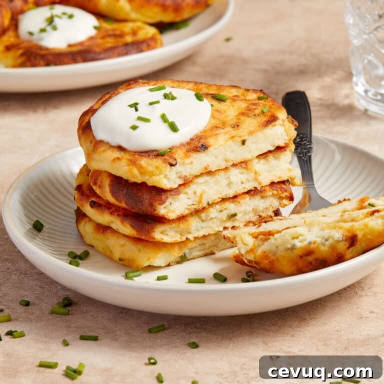 Stack of air fryer potato cakes on a plate with a dollop of sour cream and chopped chives on top.