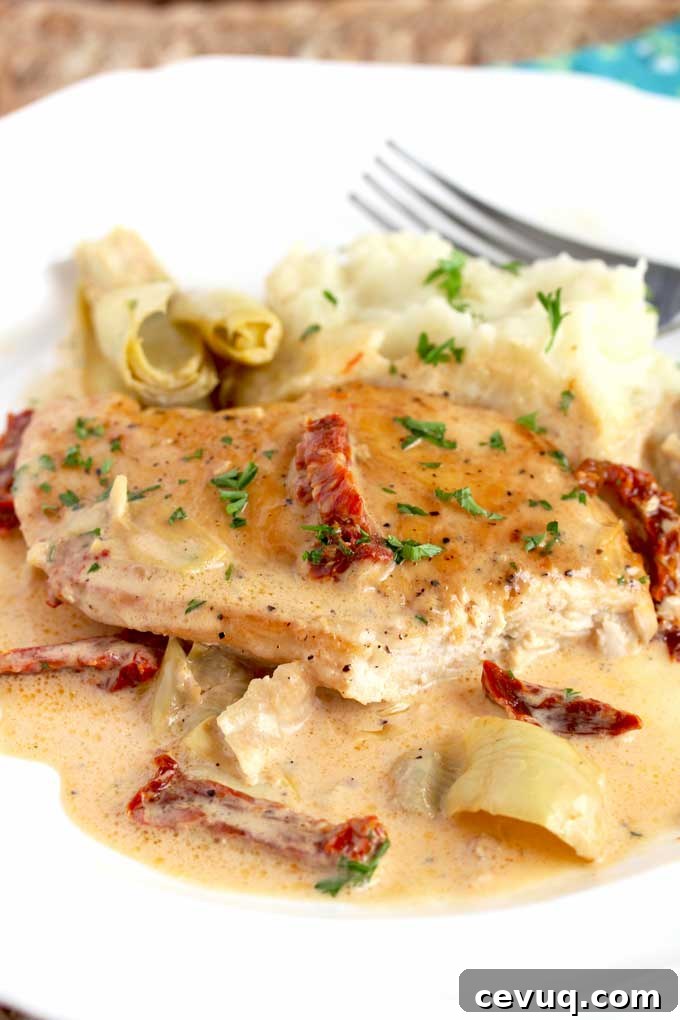 Creamy Sun-Dried Tomato Chicken with Garlic and Herbs 8 A piece of creamy chicken with artichoke hearts and sundried tomatoes on a white plate.