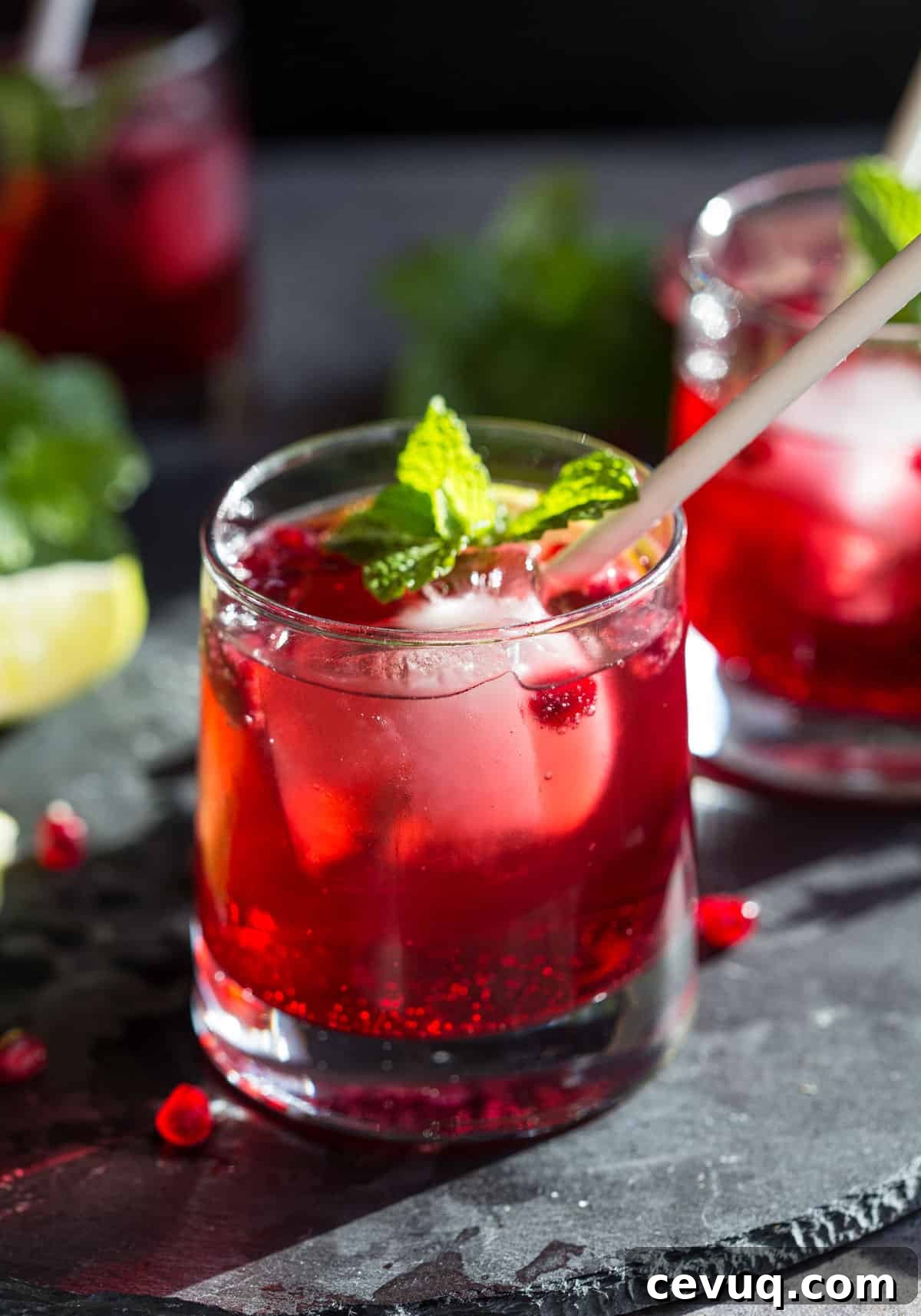 Ginger Pomegranate Spritz cocktail in a glass with a straw and fresh mint garnish