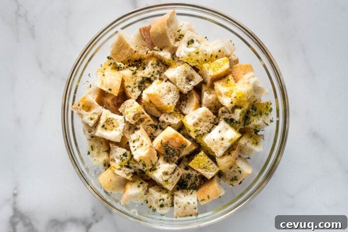 Olive oil, butter, and seasoning drizzled on bread cubes.