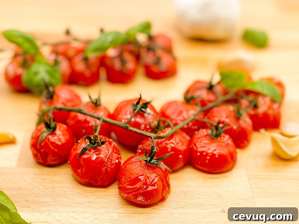 Roasted cherry tomatoes on the vine with roasted garlic cloves and fresh basil leaves on a wooden butcher block cutting board