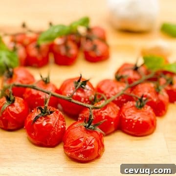 Roasted cherry tomatoes on the vine with roasted garlic cloves and fresh basil leaves on a wooden butcher block cutting board