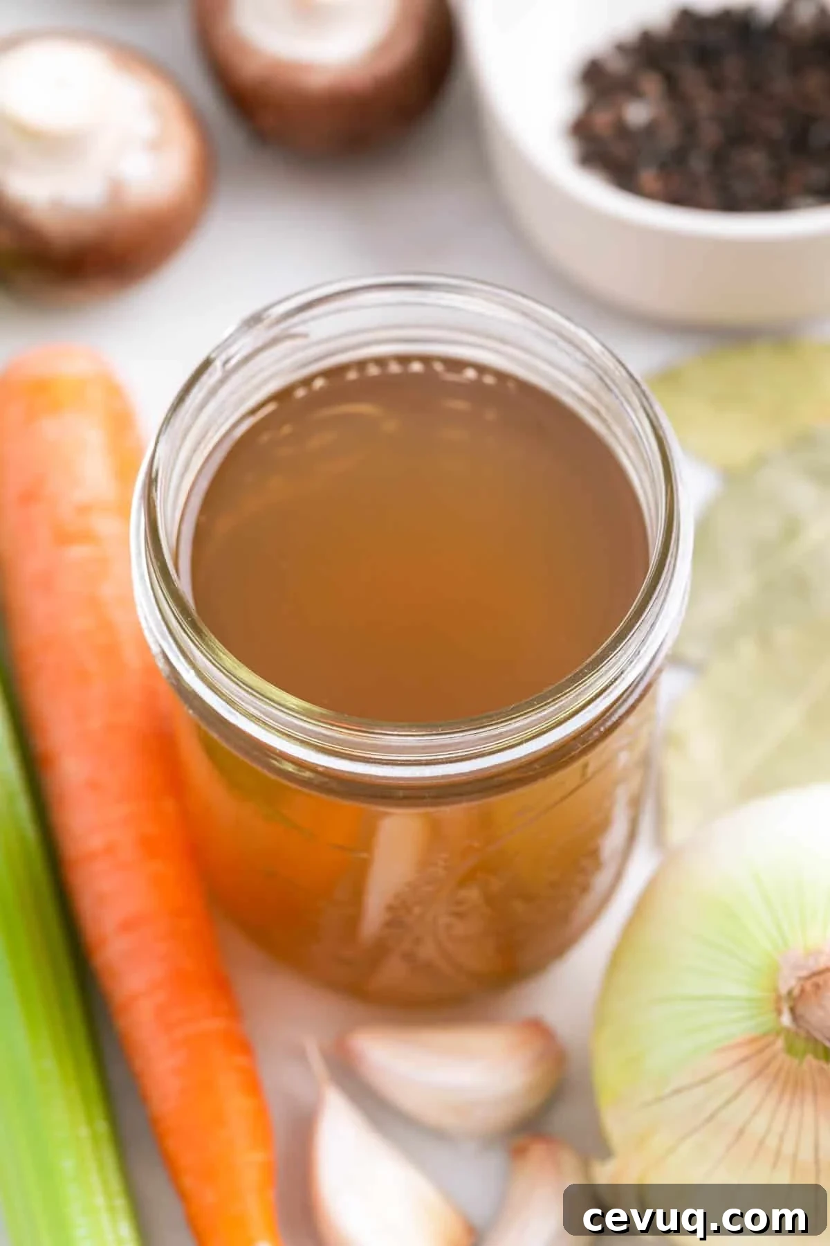 Glass jar with homemade vegetable broth and ingredients around it