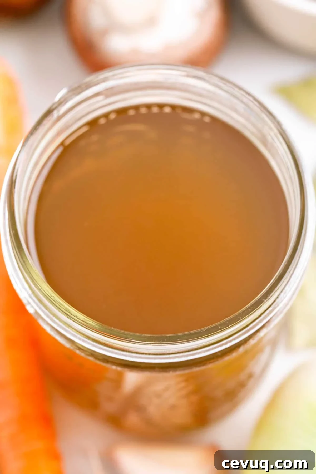 Homemade vegetable broth in a jar with vegetables and herbs around it